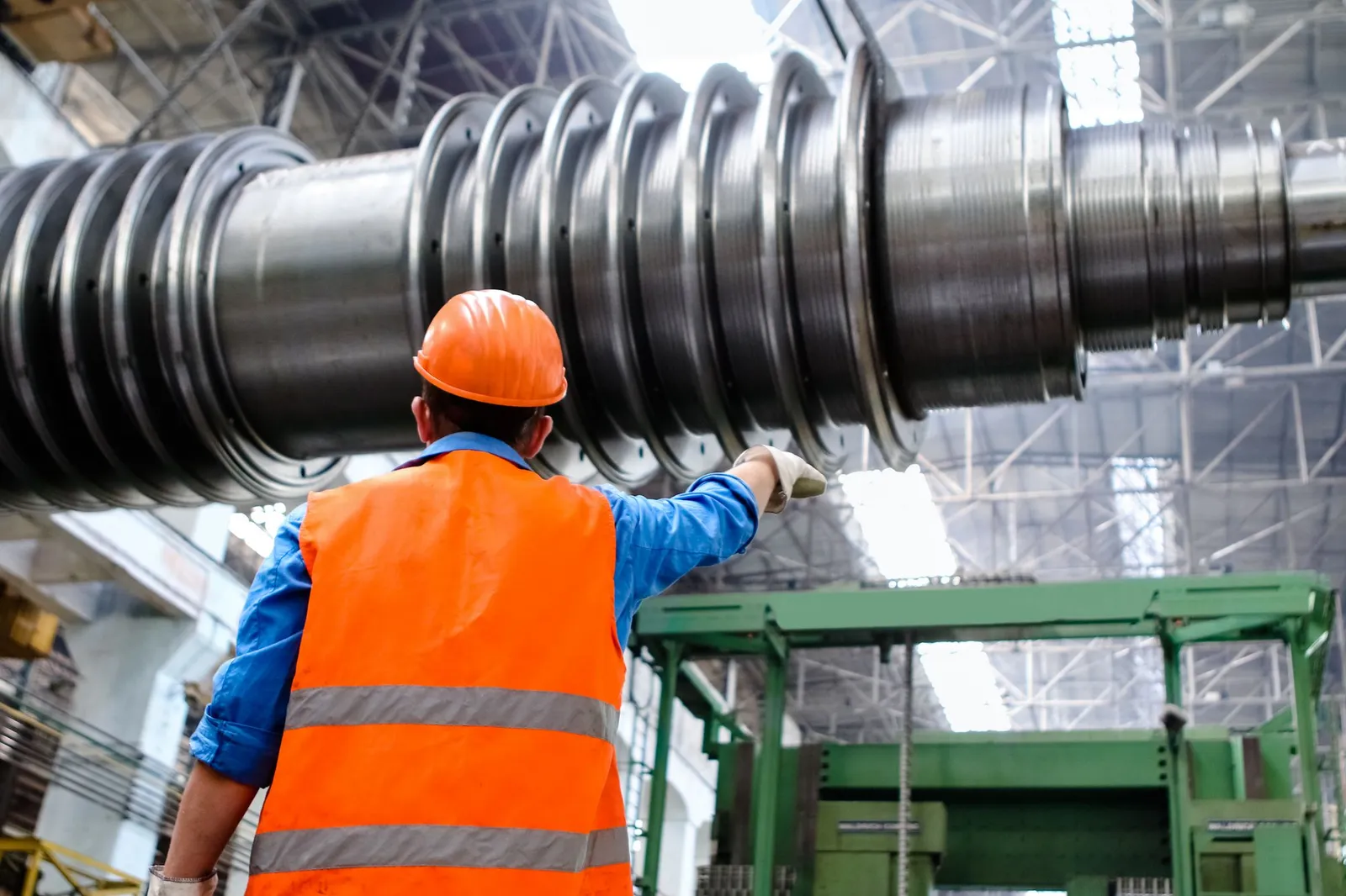 Worker in a hard hat and orange vest pointing at a large turbine rotor